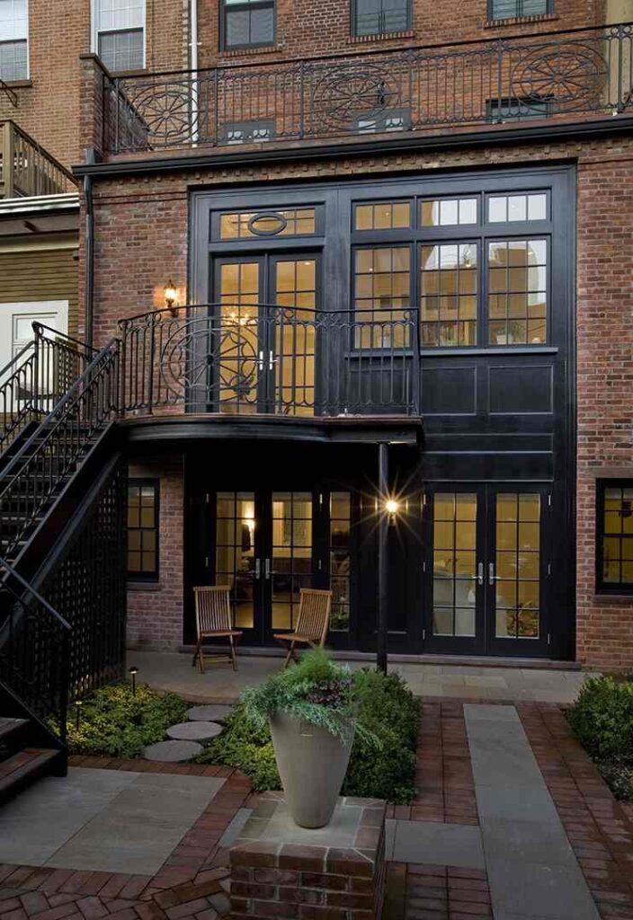 Red brick house with black trim windows and glass door and chair outside of the house