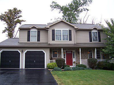 Tan house with red door and white pillars and garden outside of the house