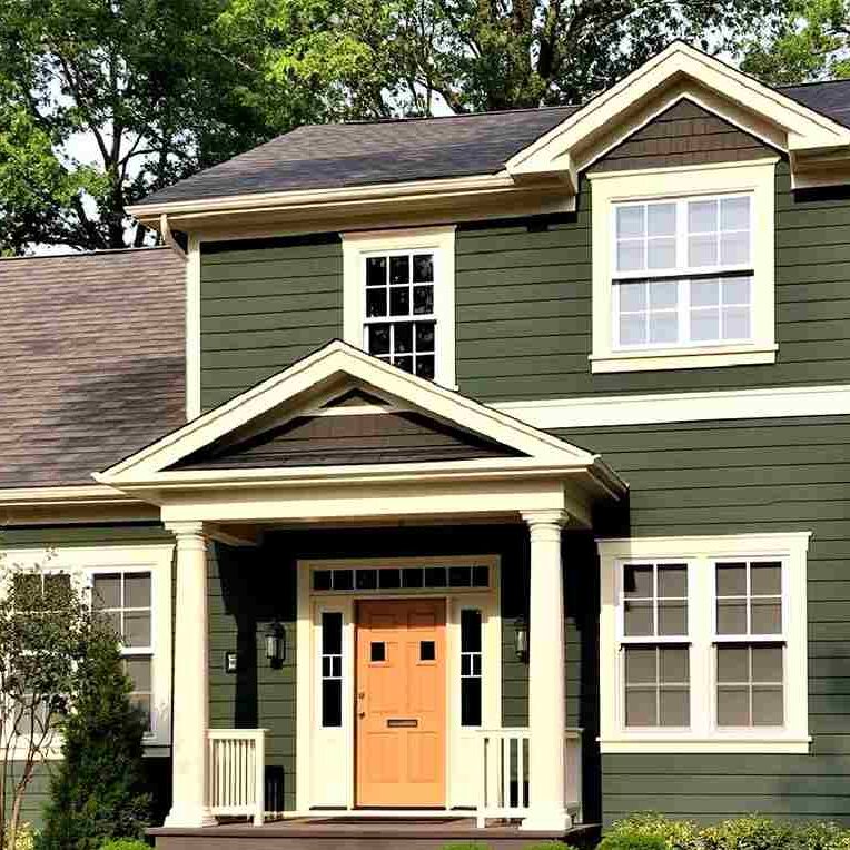 A dark green house with white trim and wooden door and white pillars