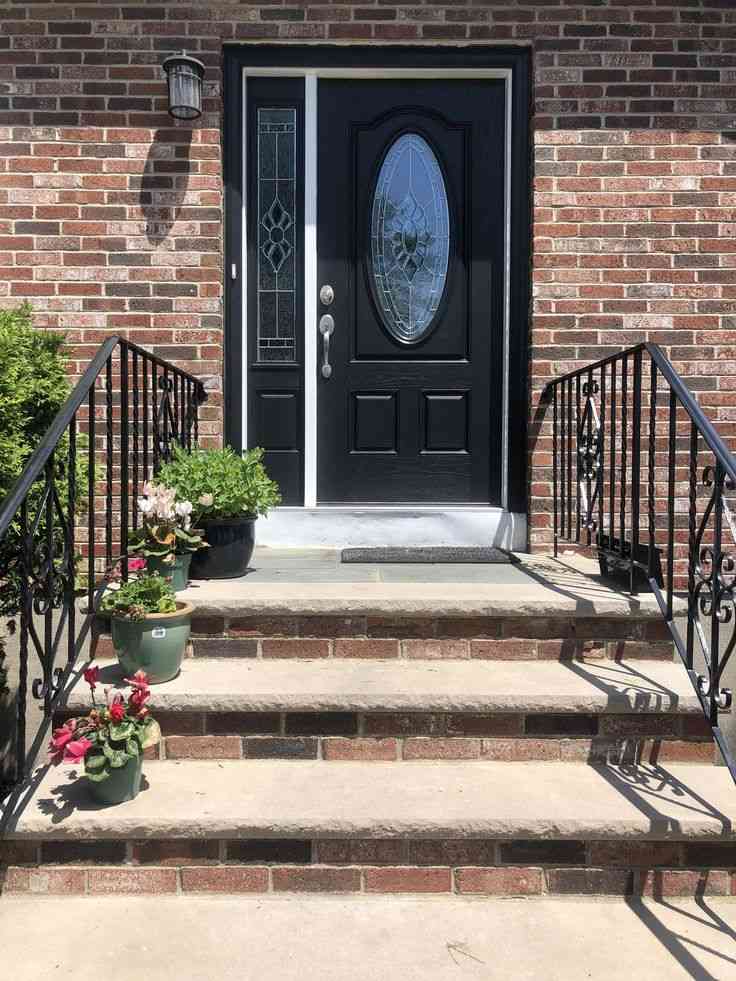 Red brick house with black front door and brick stair and black railing
and celling light on the wall