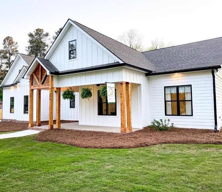 Small white house with black trim and wood and garden outside of the house