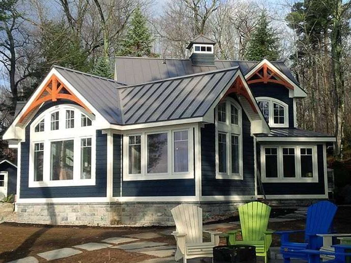 Blue house with white trim and black metal roof and chairs outside of the house