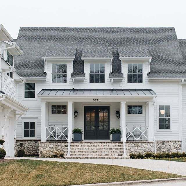 A white house with stone baseand stairs and garden outside of the house and lights on the wall