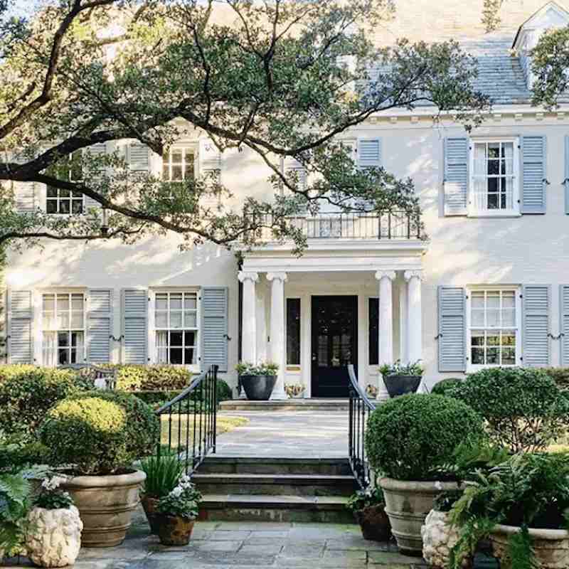 Stone pathway and white house with blue shutters and black railing and stairs