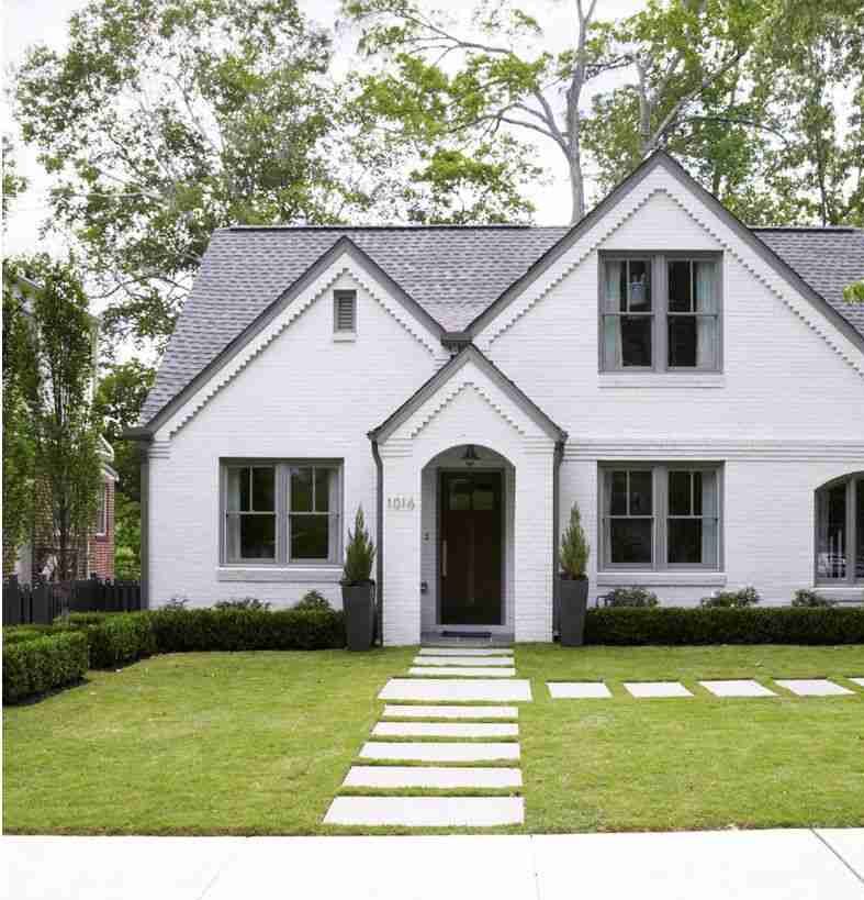 A white house with a stone pathway and windows and garden outside of the house