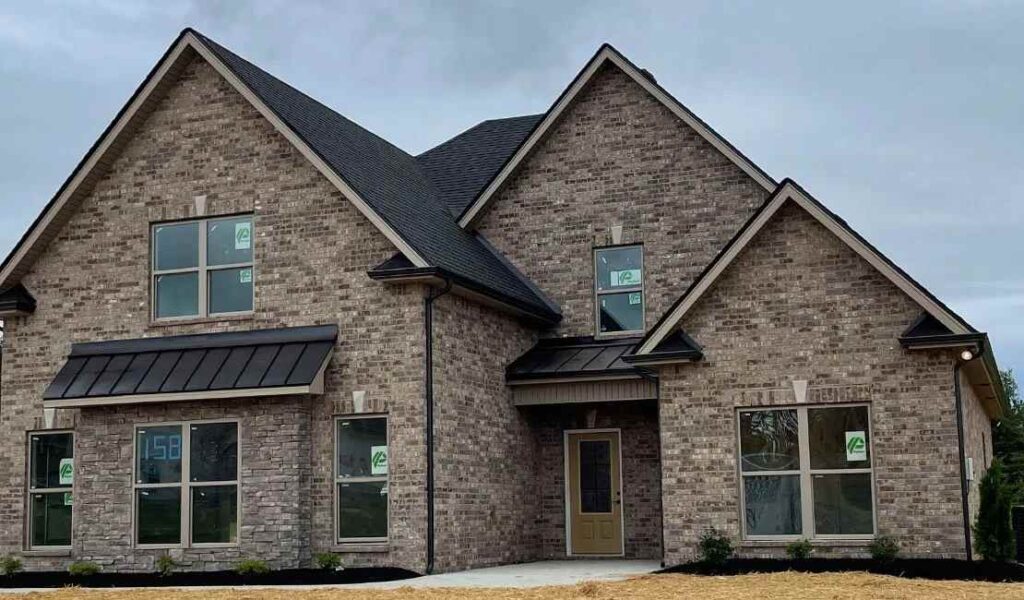 Tan brick house with black trim and roof and utters and glass windows 