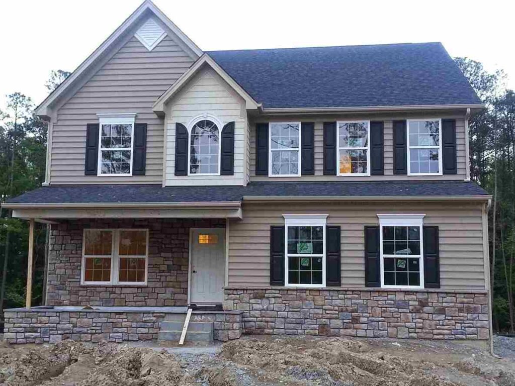 A tan brick house with black roof and black shutter