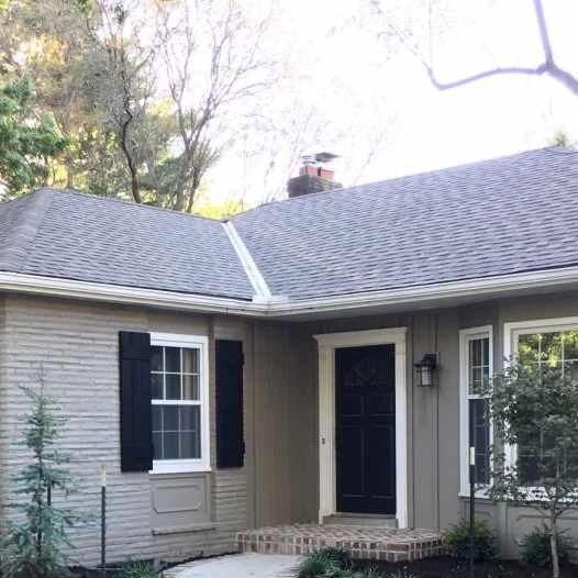 A tan house with black door and shutter and light on the wall