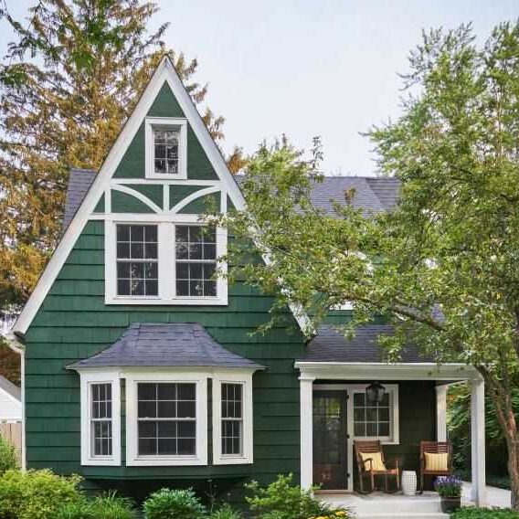 Tudor-style green house with white roofline and chairs outside of the house