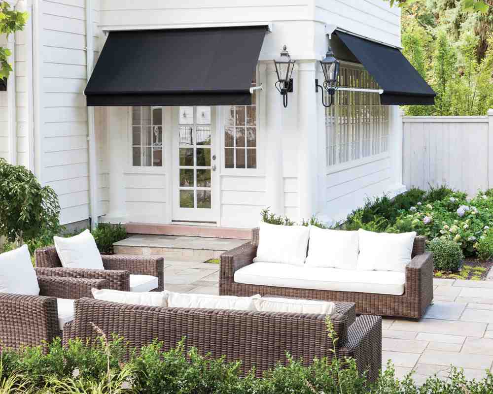 White house with black awning and glass windows and sofa outside of the house 