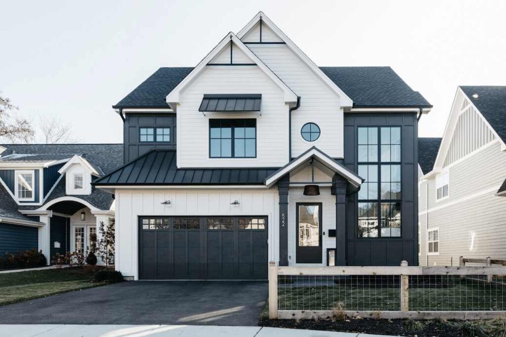 A white house with black sidling and glass windows and garage door  