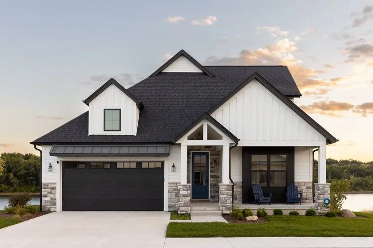 A white house with black garage door and stone base pillars