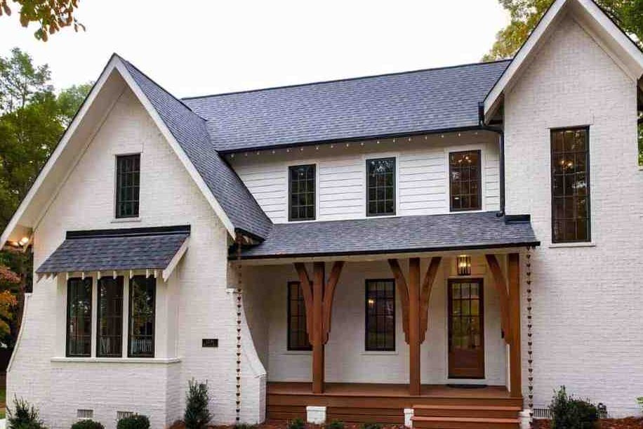 White house with wooden pillars and black trim windows and black roof