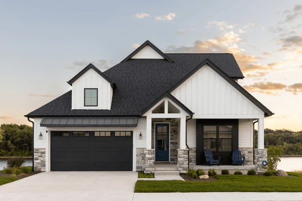 A white house with black roof and chairs outside of the house
