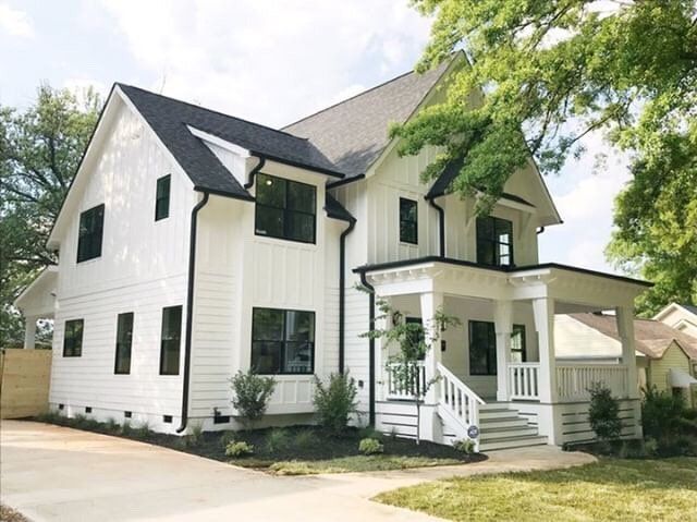 A white house with black gutter and downspouts and black windows and white balcony