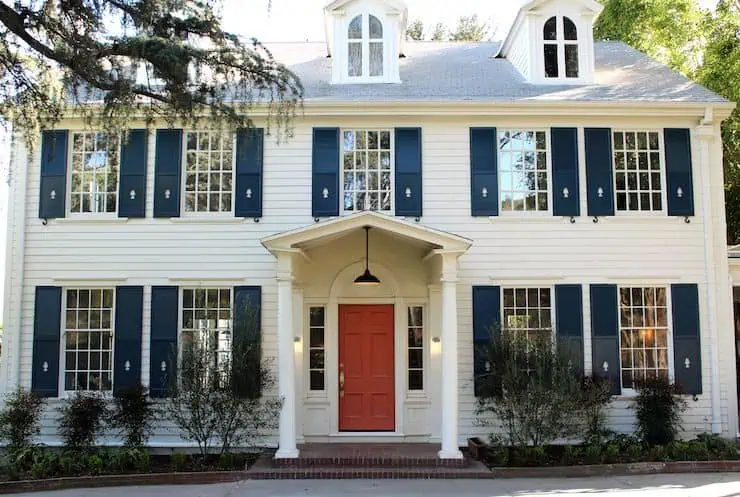 A white house with grey roof and blue shutter and red door