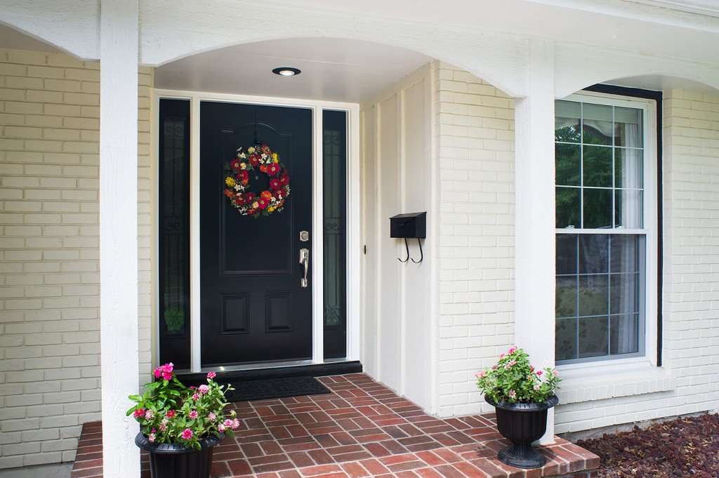 A white house with wooden porch and black front door and plants outside of the house