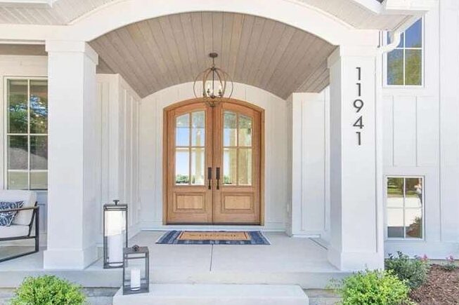 White house with wooden door and house number on the wall and lamp above the wall