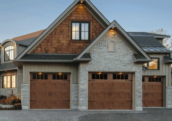 Grey stone house with wooden garage and lights on wall