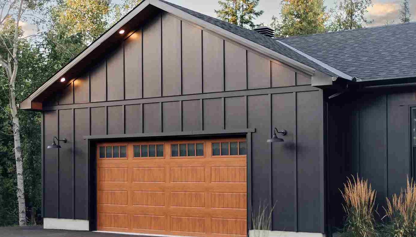 A grey house with wooden garage door and lights on the wall 