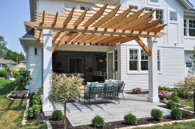 A white house with wooden pergola and chair outside of the house and white trim windows