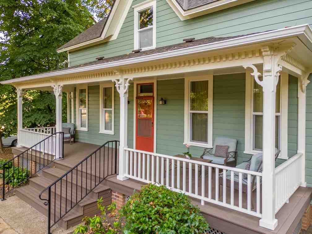 Green house with wooden porch and black railing and white balcony