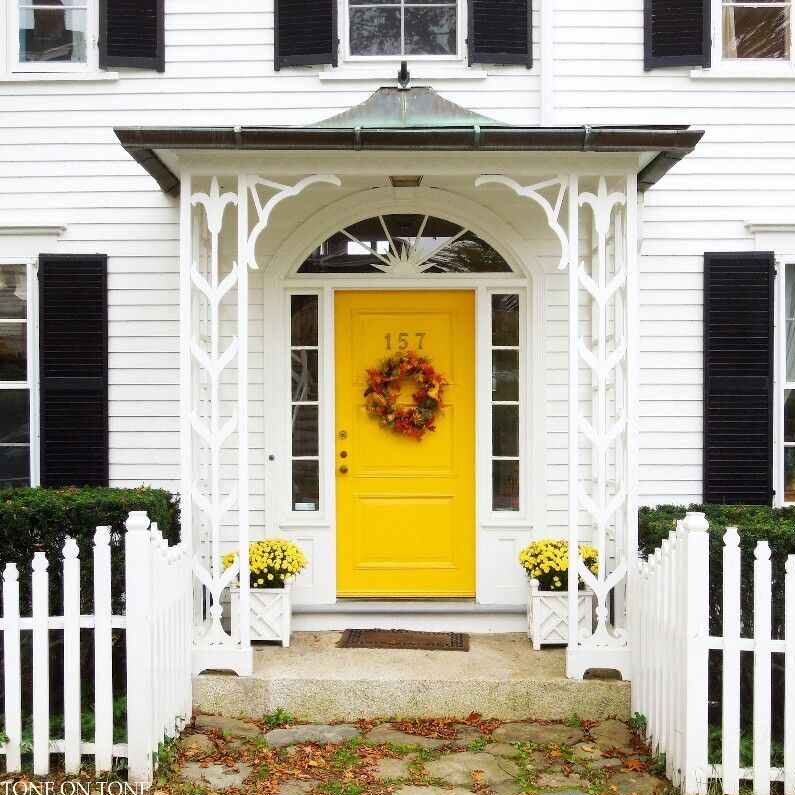 A white house with yellow front door and black trim and flowers pots outside of the house
