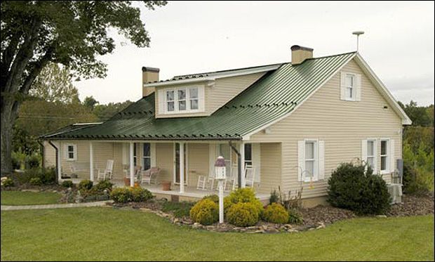 Green roof on beige house and white trim windows and garden outside of the house