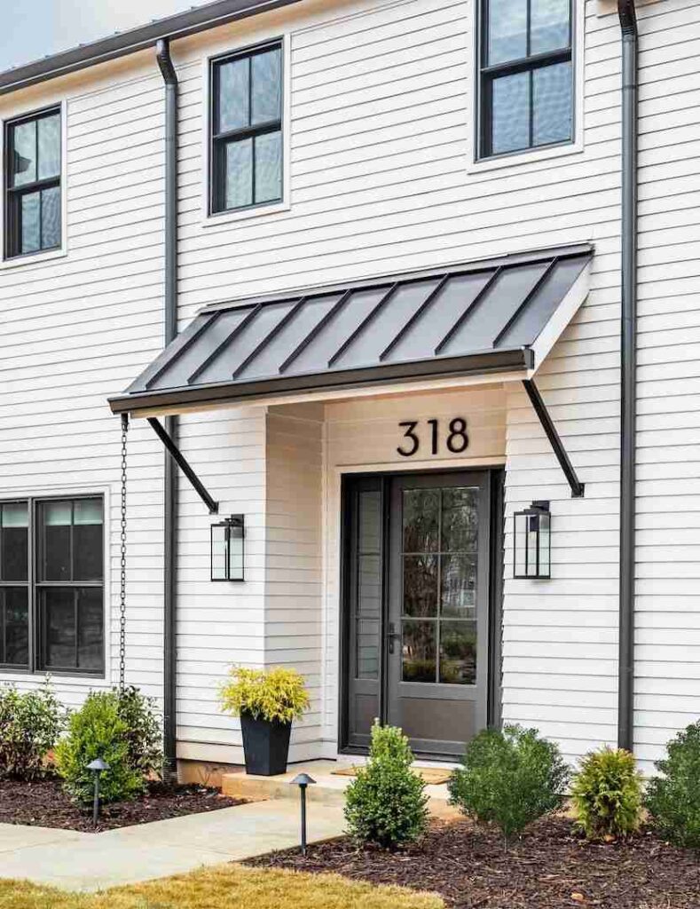 Black awnings on white house and black door and lights on the wall