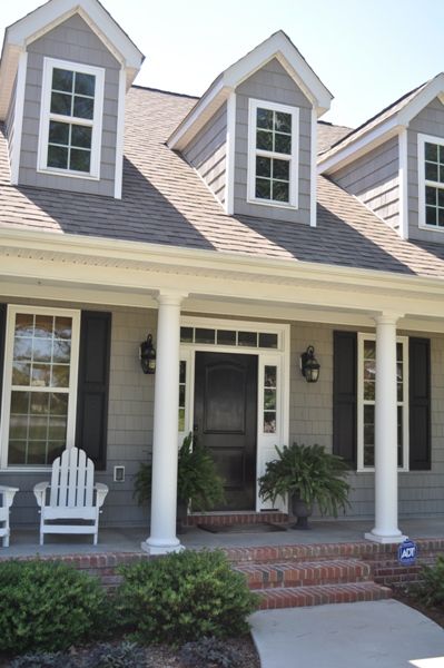 Black front door on grey house and white chairs outside of the house and white pillars and white trim windows