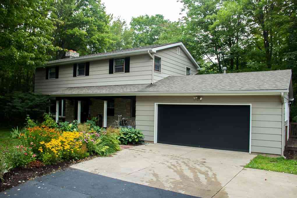 A garage black  door and green house and a pathway and fowers on the side of house 