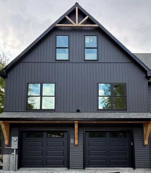 A dark grey house with black garage door and glass windows 