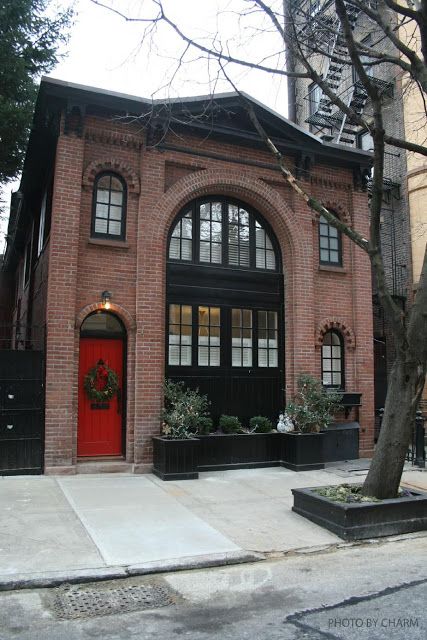 Red brick house with black glass door and black trim windows and red front door and light above the door