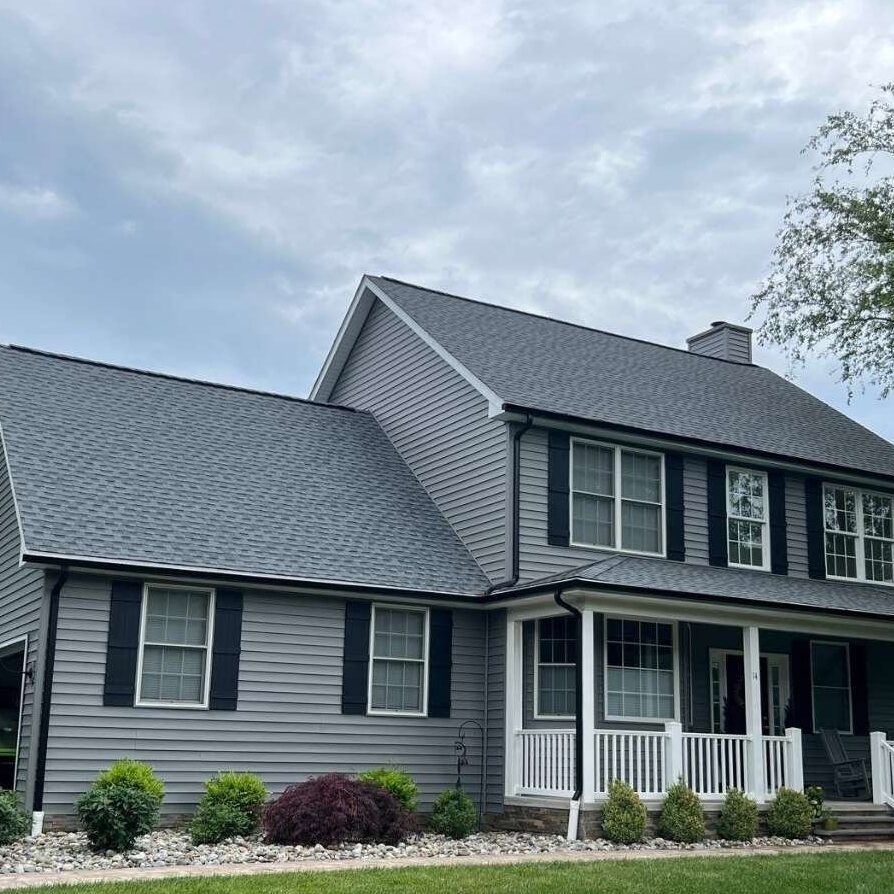 Grey house with black trim and gutter and white trim windows and garden outside of the house