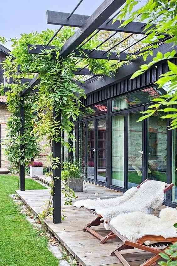 A green house with black pergola and glass windows and chars outside of the house
