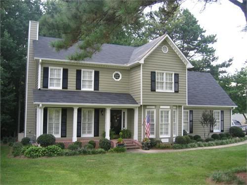 Green house with black shutter and white framed glass windows and garden outside of the house