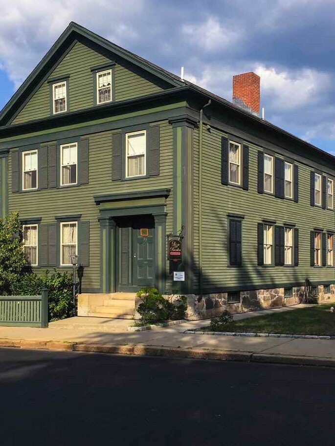 A olive green house with black trim and shutter and green pillars and white framed window