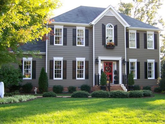 A grey house with white trim and black shutter and red door and garden outside of the house