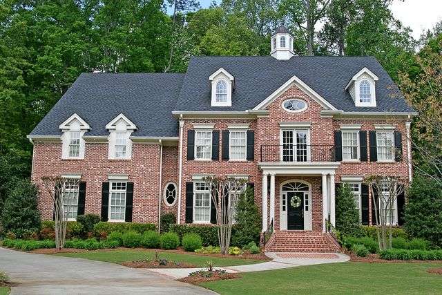 Black shutter and red brick brick house with black front door and white pillars outside of the house