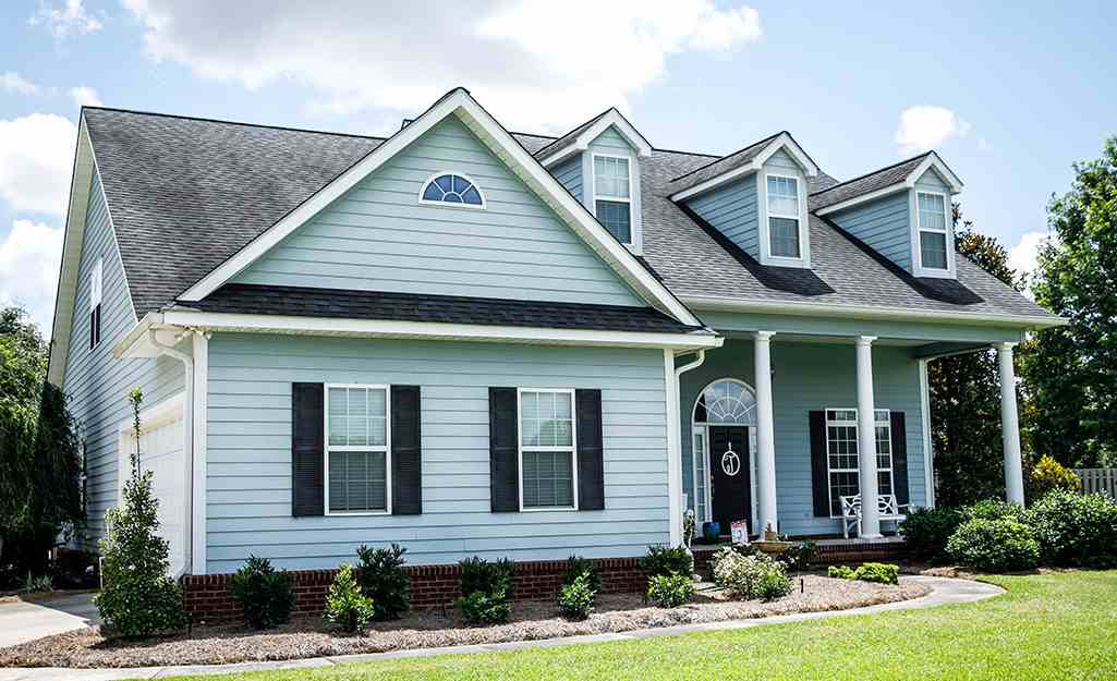 A blue house with black shutter and white trim glass windows and garden outside of the house