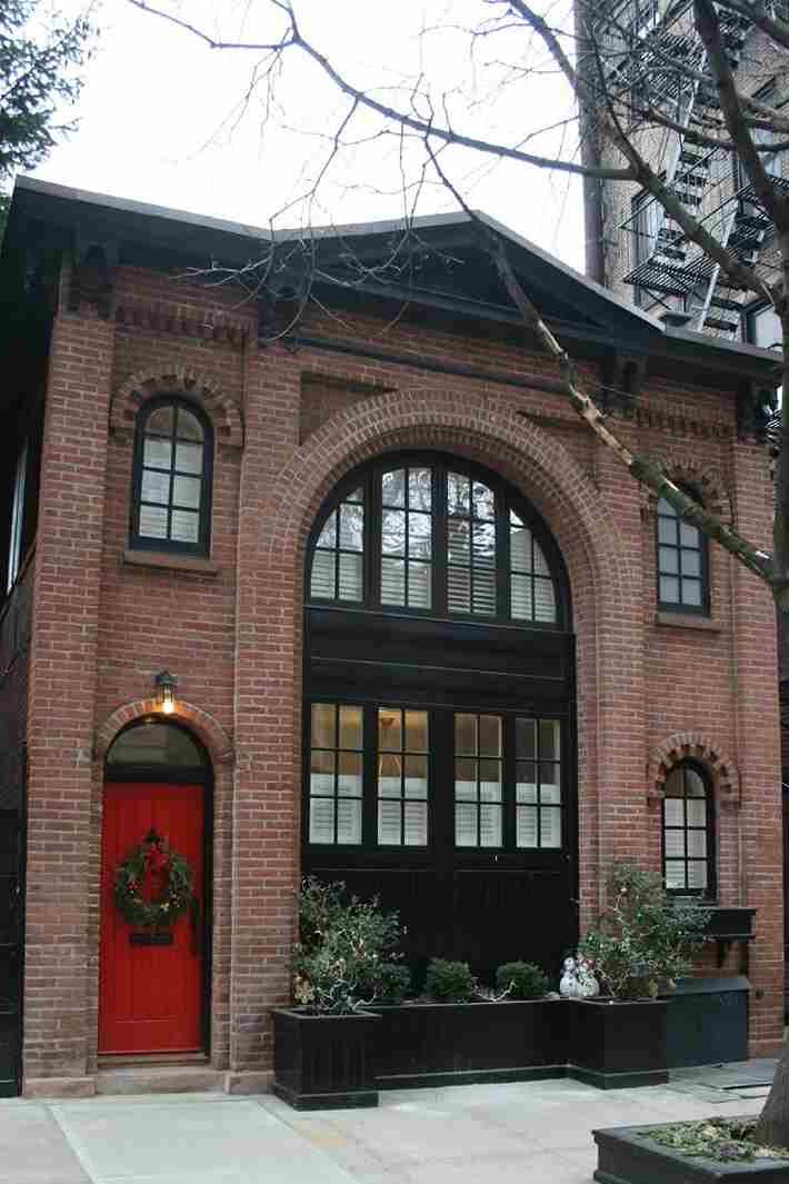 Red brick house with black trim glass windows and red door and light above the wall