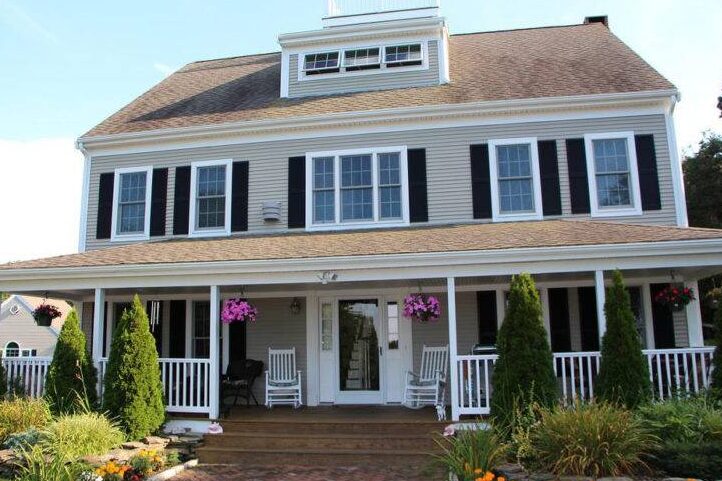 Dark brown porch house with light house and white framed windows and chair outside of the house