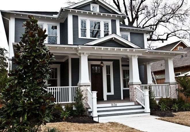 A dark grey house with white trim and white fencing around the house and black framed windows and pillars