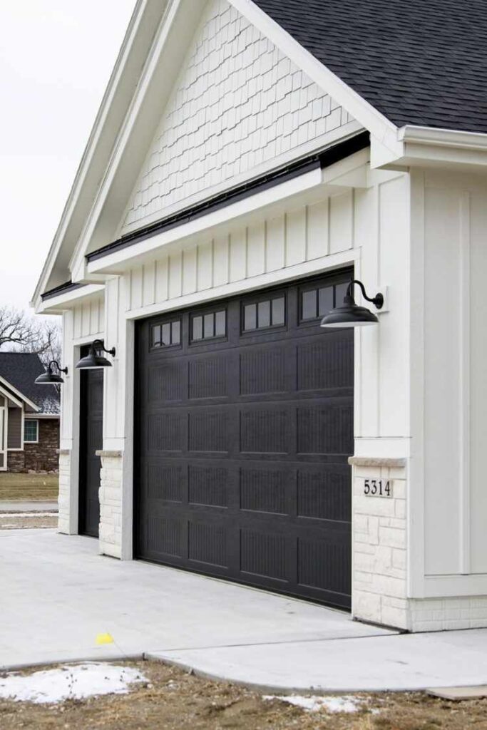 White house with black garage door and celling light on the wall