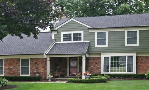 A green house with brick base and white trim house