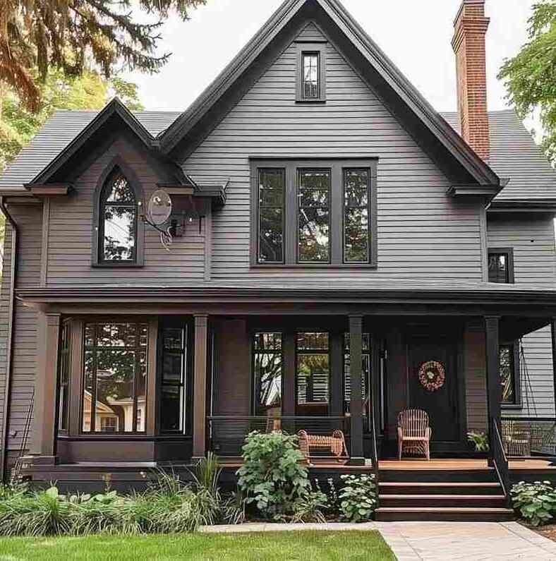 Grey house with black wood trim with glass windows and chairs outside of the house