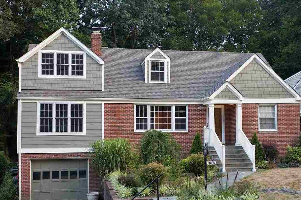 A grey stone house with red brick and white trim and staircase and white railing