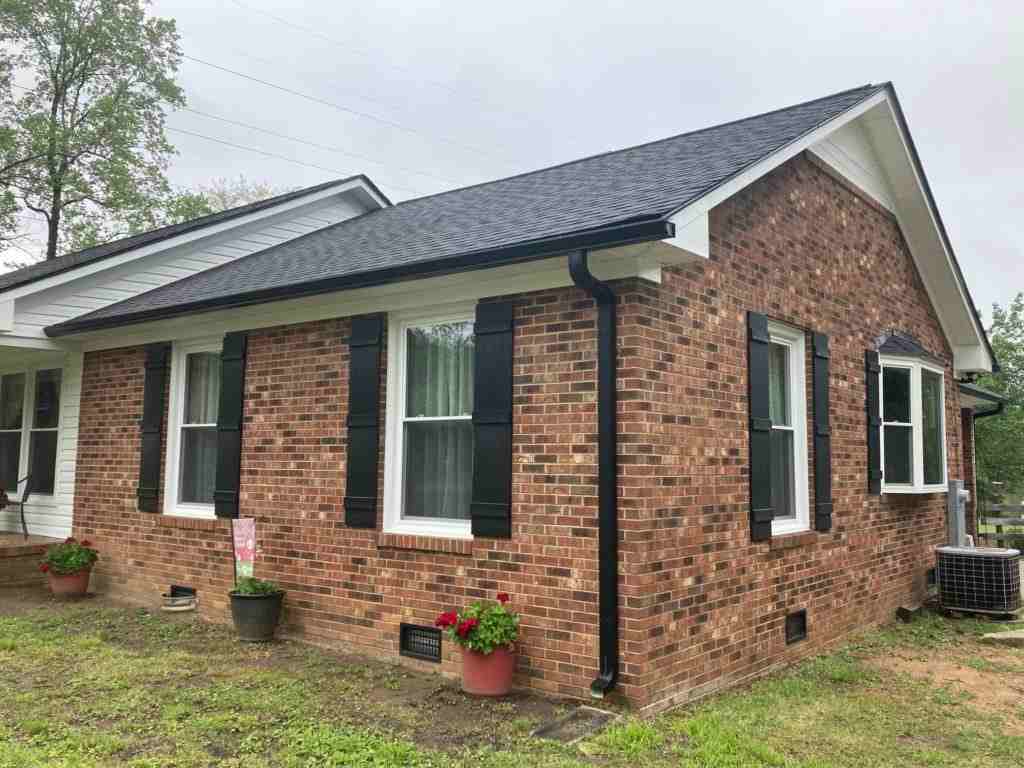Black roof and black gutters on red brick house and garden outside of the house