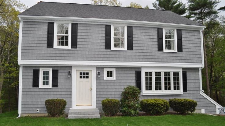 A light gray house and black gutter white trim windows and plants outside of the house 