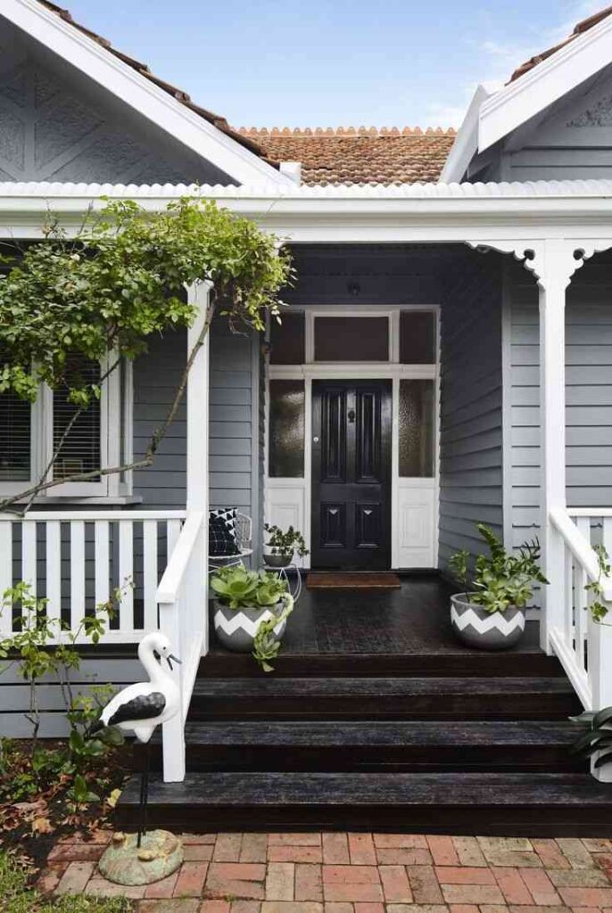 Grey house with black porch with white railing and plant pot outside of the house